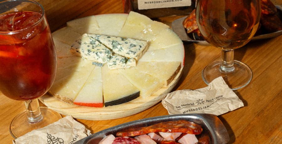 Maridaje de quesos de oveja con vermut y cerveza en mesa de madera – Museo del Jamón