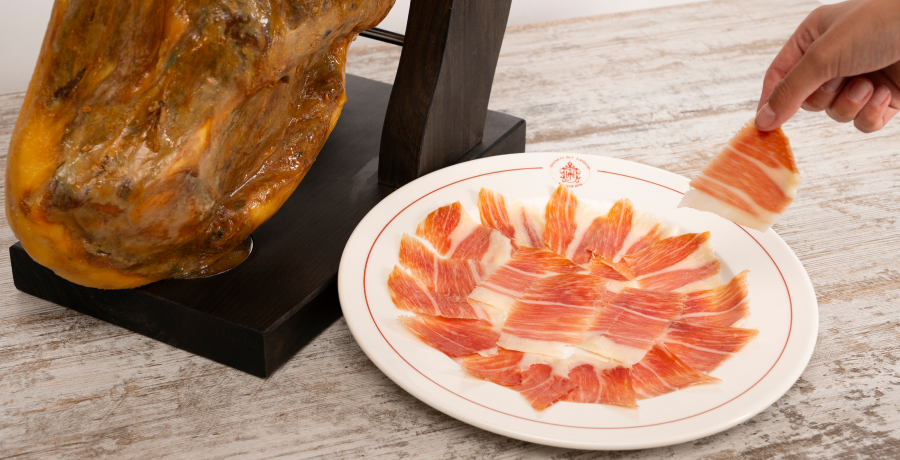 Paletilla de jamón ibérico en jamonero con plato de lonchas finas recién cortadas