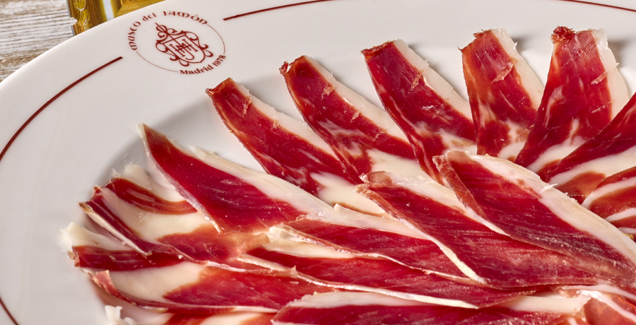 Primer plano de lonchas de jamón ibérico sobre un plato blanco de Museo del Jamón.