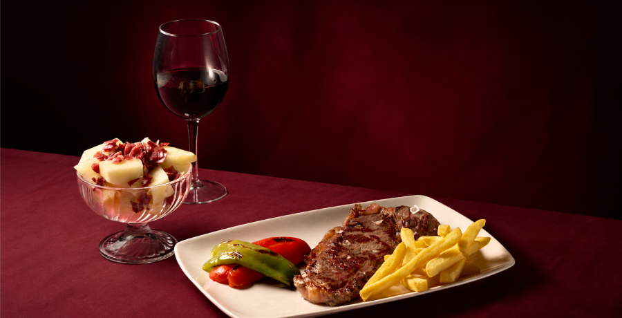 Plato de carne con patatas y pimientos, ensalada con jamón y vino para comer cerca de Atocha